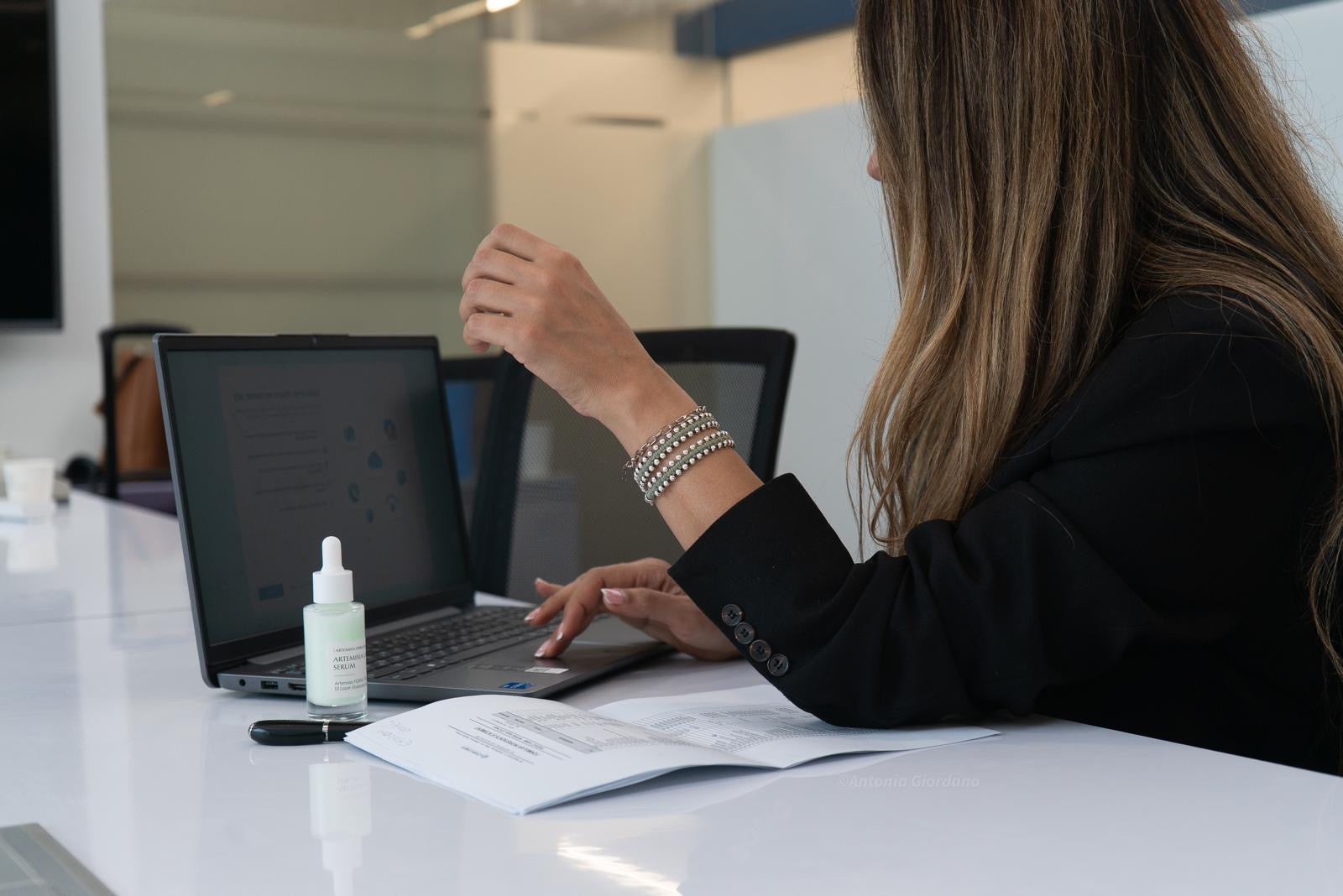 Person sitting at a desk with a laptop and a bottle of hand sanitizer.