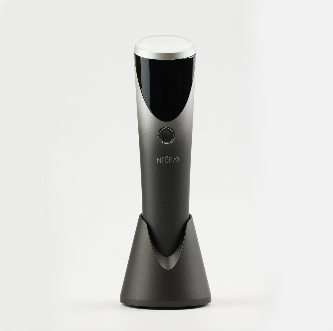 Sleek handheld INFERA device in a metallic finish, featuring a rounded treatment head, single control button, and charging stand, designed for targeted light therapy use.