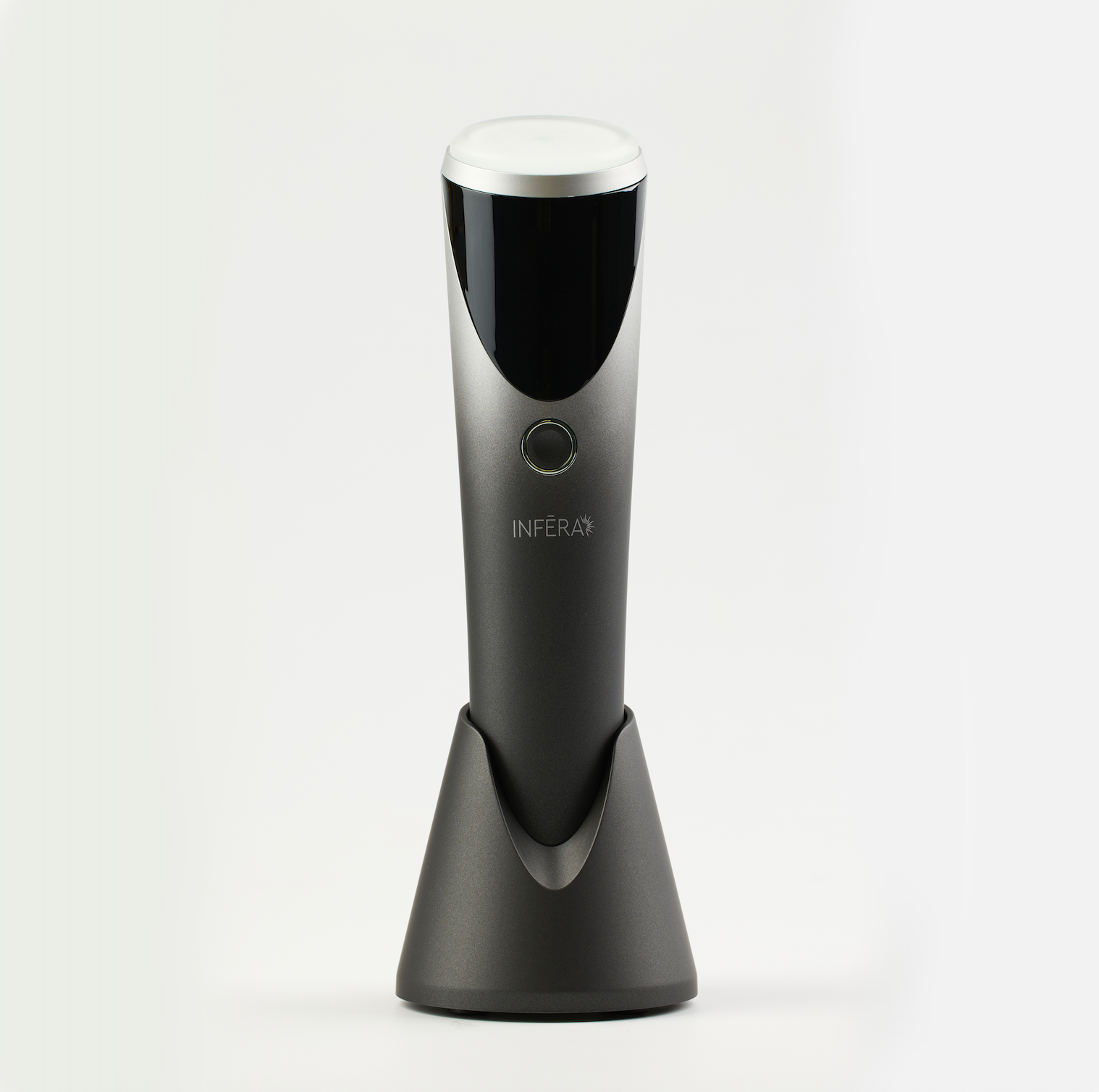 Sleek handheld INFERA device in a metallic finish, featuring a rounded treatment head, single control button, and charging stand, designed for targeted light therapy use.